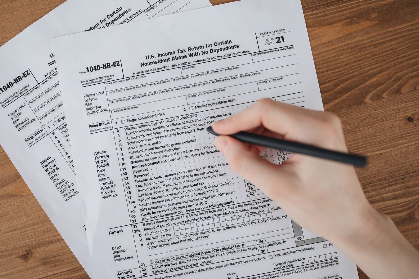 A person working through printed tax paperwork at a desk with a laptop and pen
